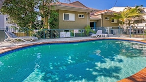 A swimming pool with lounge chairs, a fenced area, and a building with a tiled roof. - Pacific Waves (Sunrise Beach)