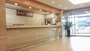 Zona de recepción de hotel con mostrador de mármol, una pantalla de reloj y un amplio ventanal que ofrece vistas a arquitectura tradicional.