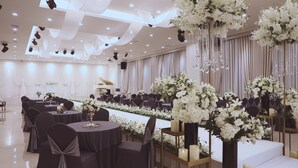 Un amplio salón de banquetes con mesas redondas, sillas negras y arreglos florales blancos.