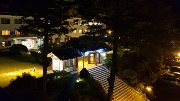 Un edificio de estilo tradicional con tejado de tejas y un pequeño porche, rodeado de árboles y un sendero bien iluminado.