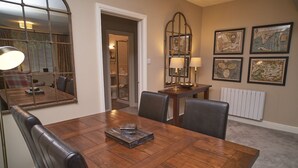 A dining area with a wooden table, chairs, and a mirror. There are framed pictures on the wall and a radiator below. - Old Bakers Cottage, ground floor centrally located cottage in the heart of Grasmere. (Ambleside)