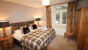 A bedroom with a bed, two bedside tables, a chair, a wardrobe, and a window with curtains. - Old Bakers Cottage, ground floor centrally located cottage in the heart of Grasmere. (Ambleside)