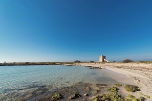 Paisagem costeira com águas cristalinas, uma praia arenosa e uma estrutura de torre histórica.