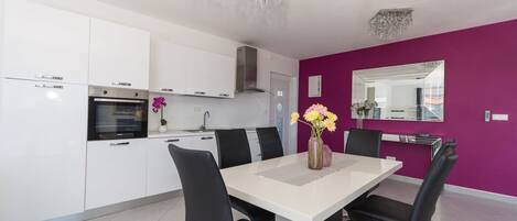 A modern kitchen with white cabinets, a dining table with black chairs, and a purple accent wall.