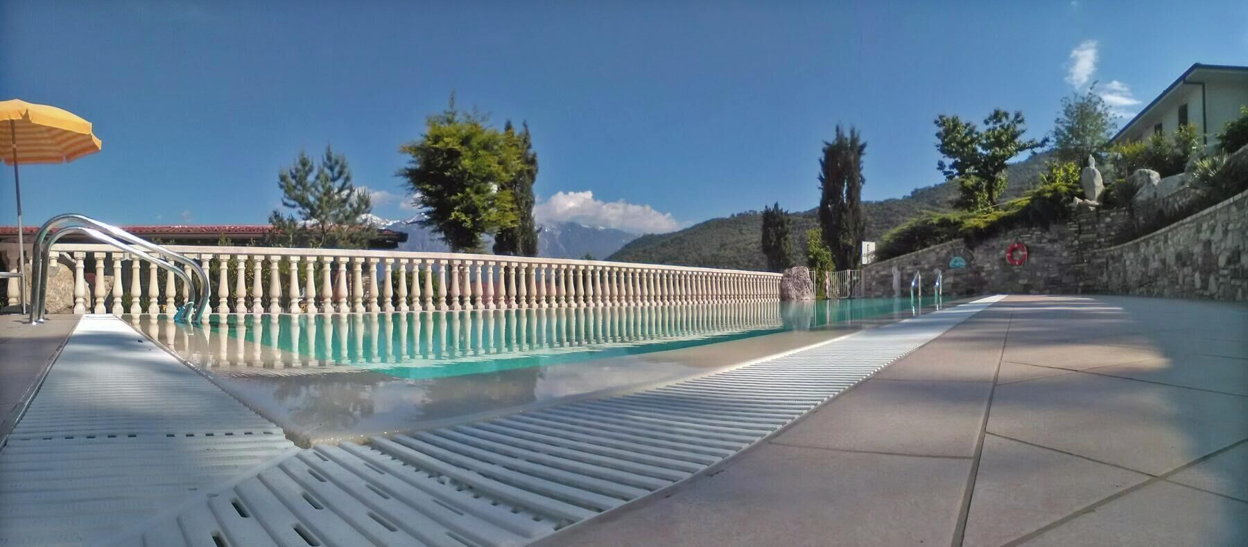 A swimming pool with a metal railing, a yellow umbrella, and a stone wall in the background.