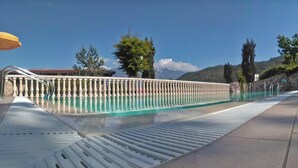Ein Swimmingpool mit Metallgeländer, einem gelben Sonnenschirm und einer Steinmauer im Hintergrund.