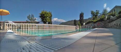 A swimming pool with a metal railing, a yellow umbrella, and a stone wall in the background.