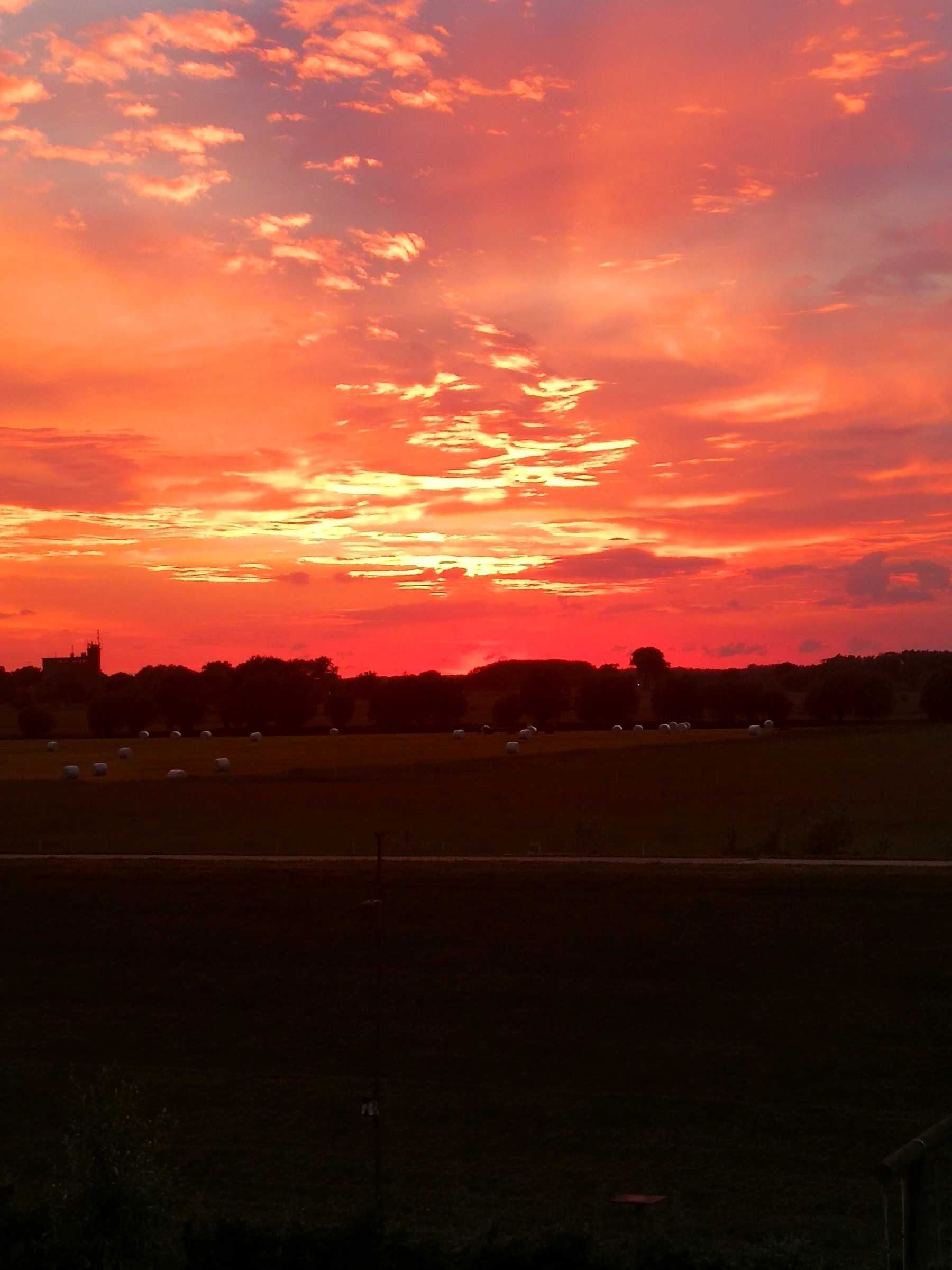 A sunset over a rural landscape with fields and a distant building.
