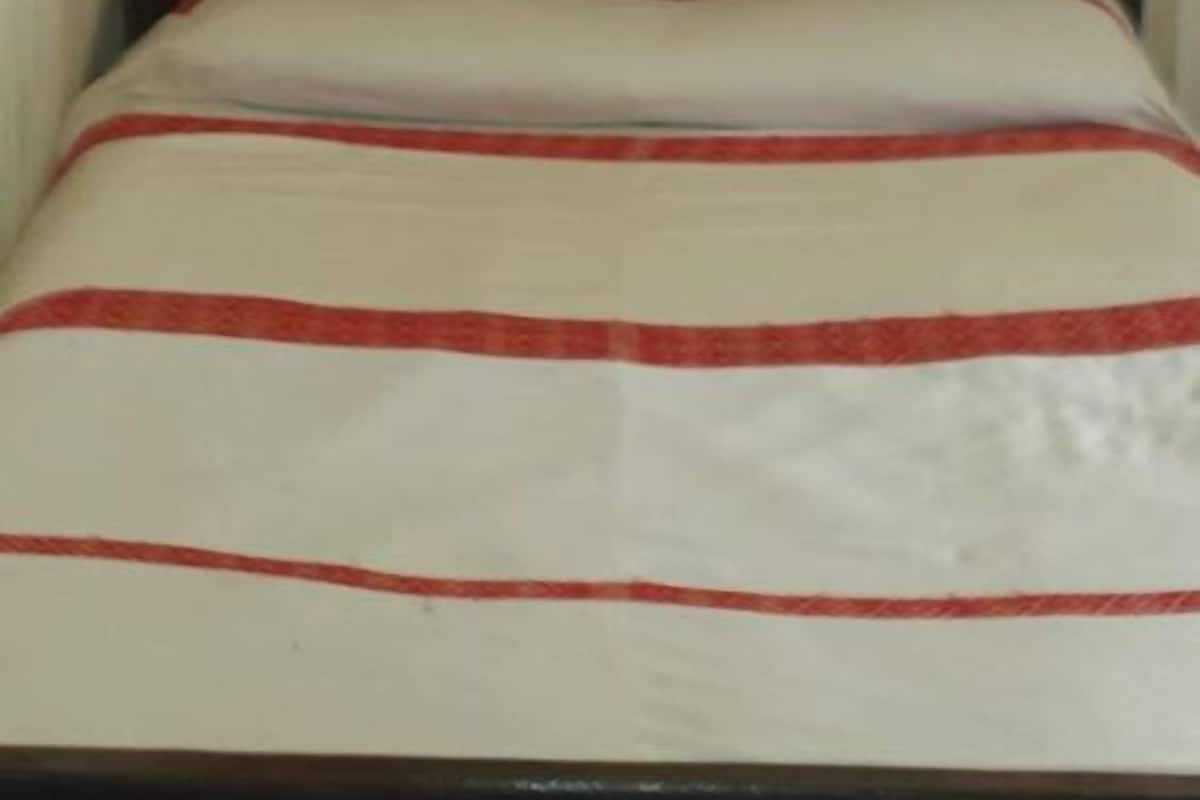 Ein Bett mit einem gemusterten Kopfteil und einer weißen Bettdecke mit roten Streifen.