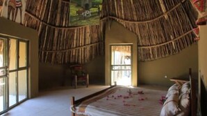 A room with a thatched roof, a bed with pillows, a painting on the wall, and a window. - Emerald Lodge Turmi (Turmi)