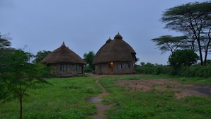 Two thatched-roof huts with a dirt path leading to them, surrounded by greenery. - Emerald Lodge Turmi (Turmi)