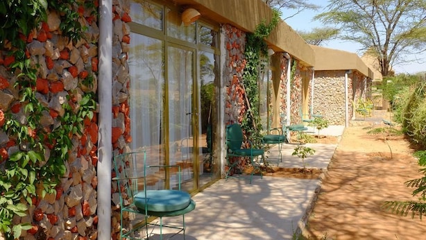 A building with a stone facade, large glass windows, and a covered outdoor seating area with chairs. - Emerald Lodge Turmi (Turmi)
