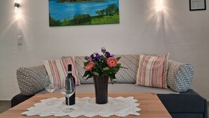 Un salon avec un canapé, une table ornée d’un vase de fleurs, une bouteille de vin et deux lampes fixées au mur.