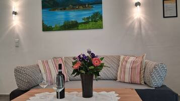 A living room with a sofa, a table with a vase of flowers, a wine bottle, and two wall-mounted lights.