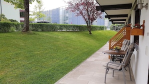 Une pelouse bien entretenue, une terrasse avec des meubles d’extérieur et un bâtiment moderne en arrière-plan.
