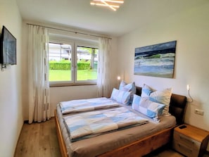 Une chambre à coucher avec un lit, des rideaux, un tableau, une télévision et une table de chevet.