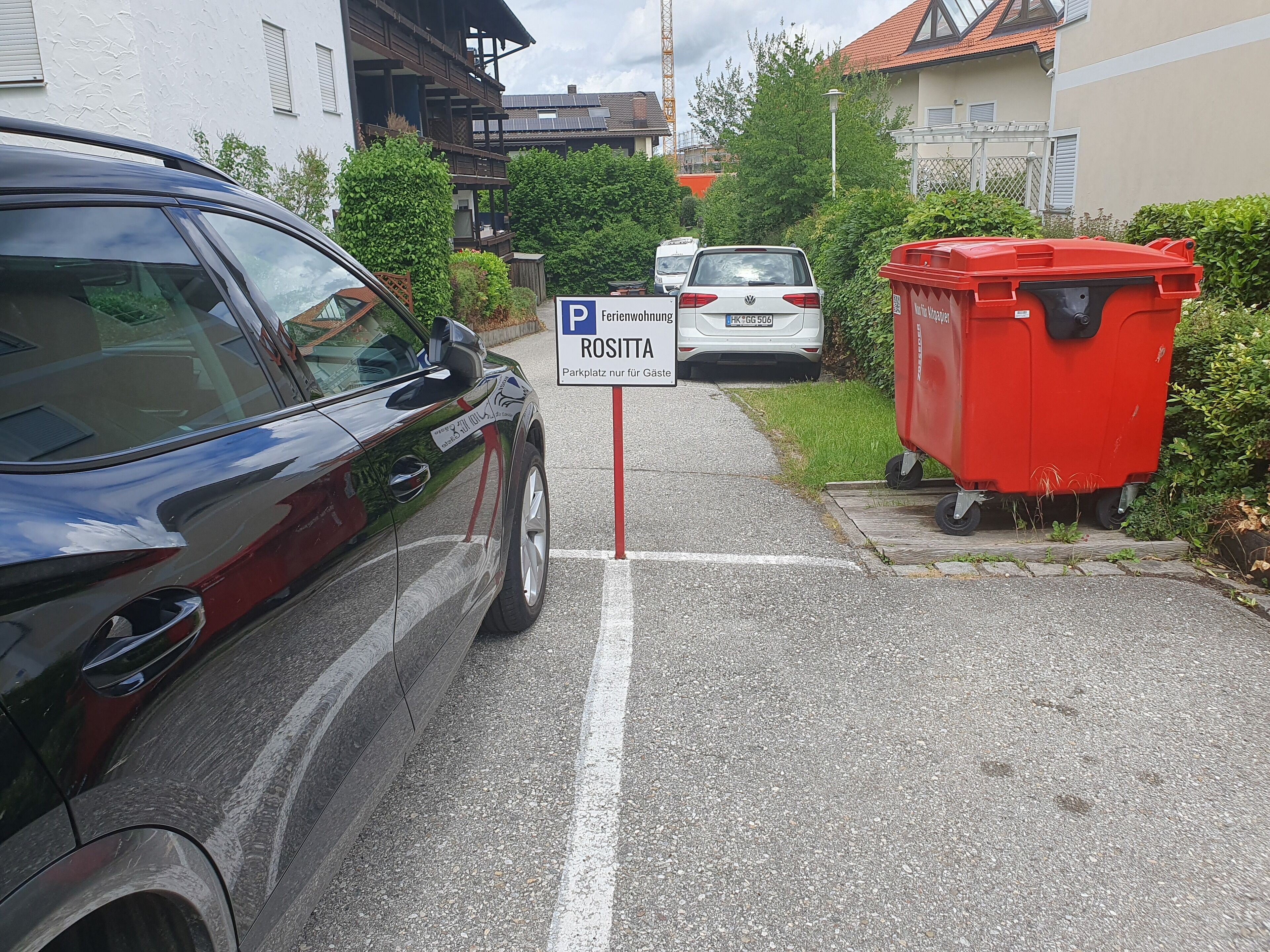 A parking sign with text in a foreign language, a red car, and a red dumpster.