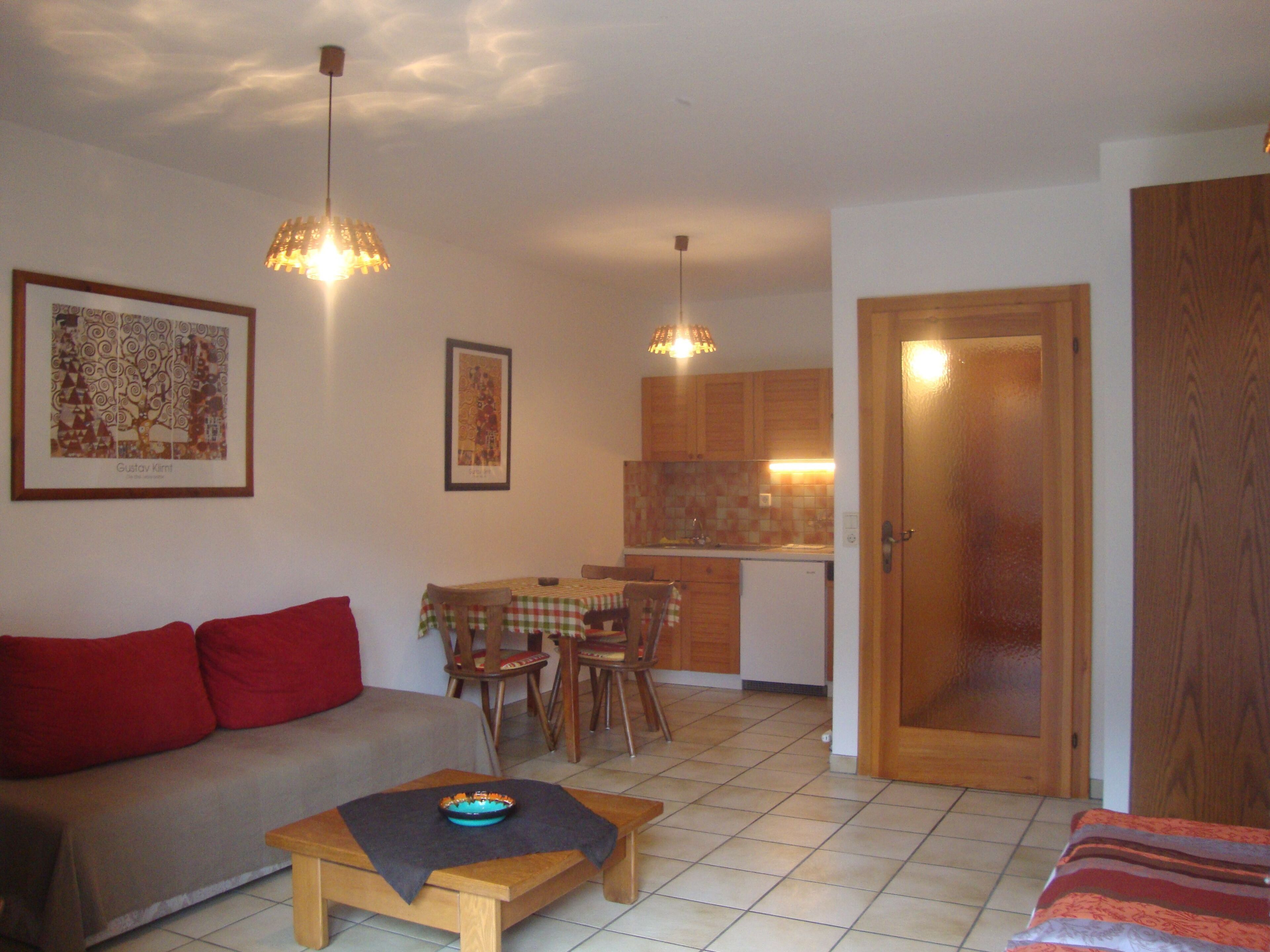 Ein Wohnzimmer mit Sofa, Couchtisch, Essbereich mit Stühlen, einer Küche mit Schränken und einer Tür.