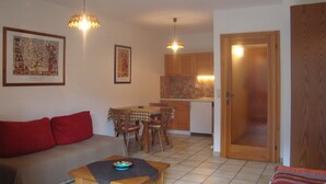 A living room with a sofa, a coffee table, a dining area with chairs, a kitchen with cabinets, and a door.