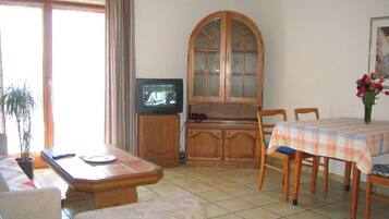 Ein Wohnzimmer mit Fernseher, Holzschrank, Esstisch und Stühlen.
