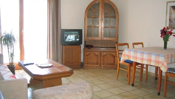 A living room with a television, wooden cabinet, dining table, and chairs.