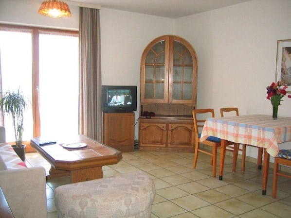 Una sala de estar con televisor, aparador de madera, mesa de comedor y sillas.