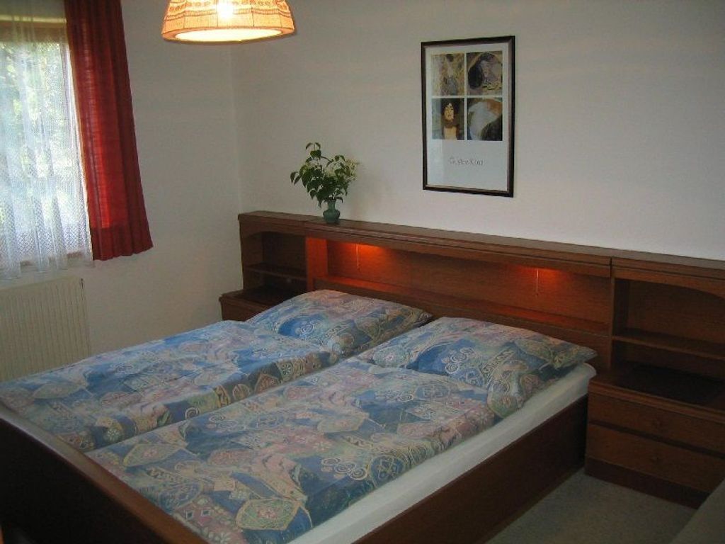 Ein Doppelbett mit gemusterten Betttextilien, ein Nachttisch, ein Wandbild und ein Fenster mit Vorhängen.