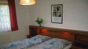 A double bed with patterned bedding, a bedside table, a wall-mounted picture, and a window with curtains.