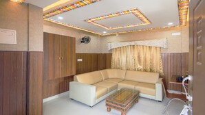 A modern living room with a sectional sofa, a glass coffee table, wooden cabinets, and a ceiling with stained glass panels. - Treebo Trend Dvaraka Inn (Bengaluru)