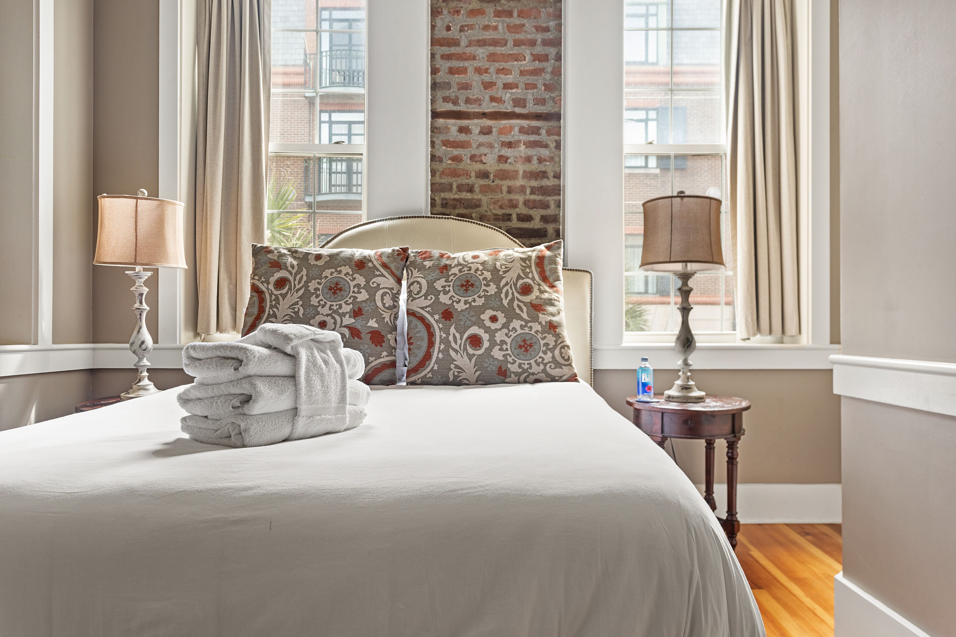 A neatly made bed with a stack of white towels, two patterned pillows, and two bedside lamps.
