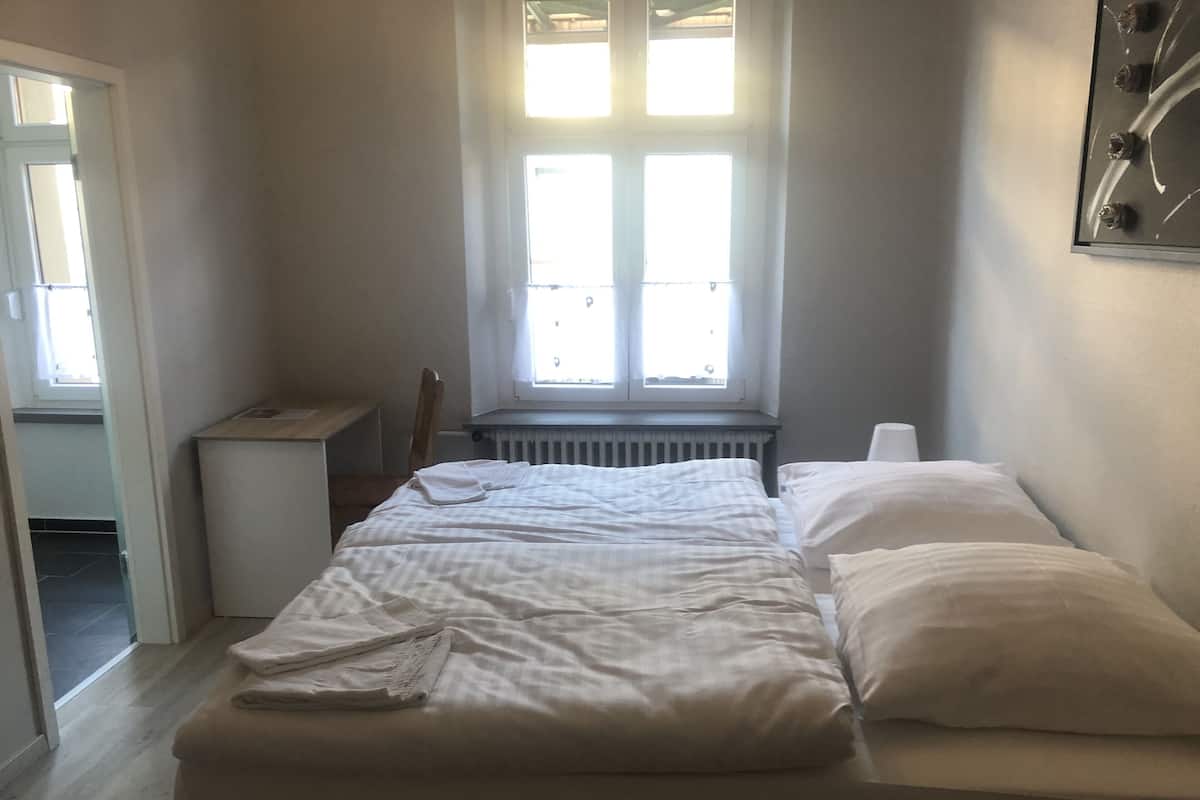 Quarto com cama, radiador, janela e escrivaninha.