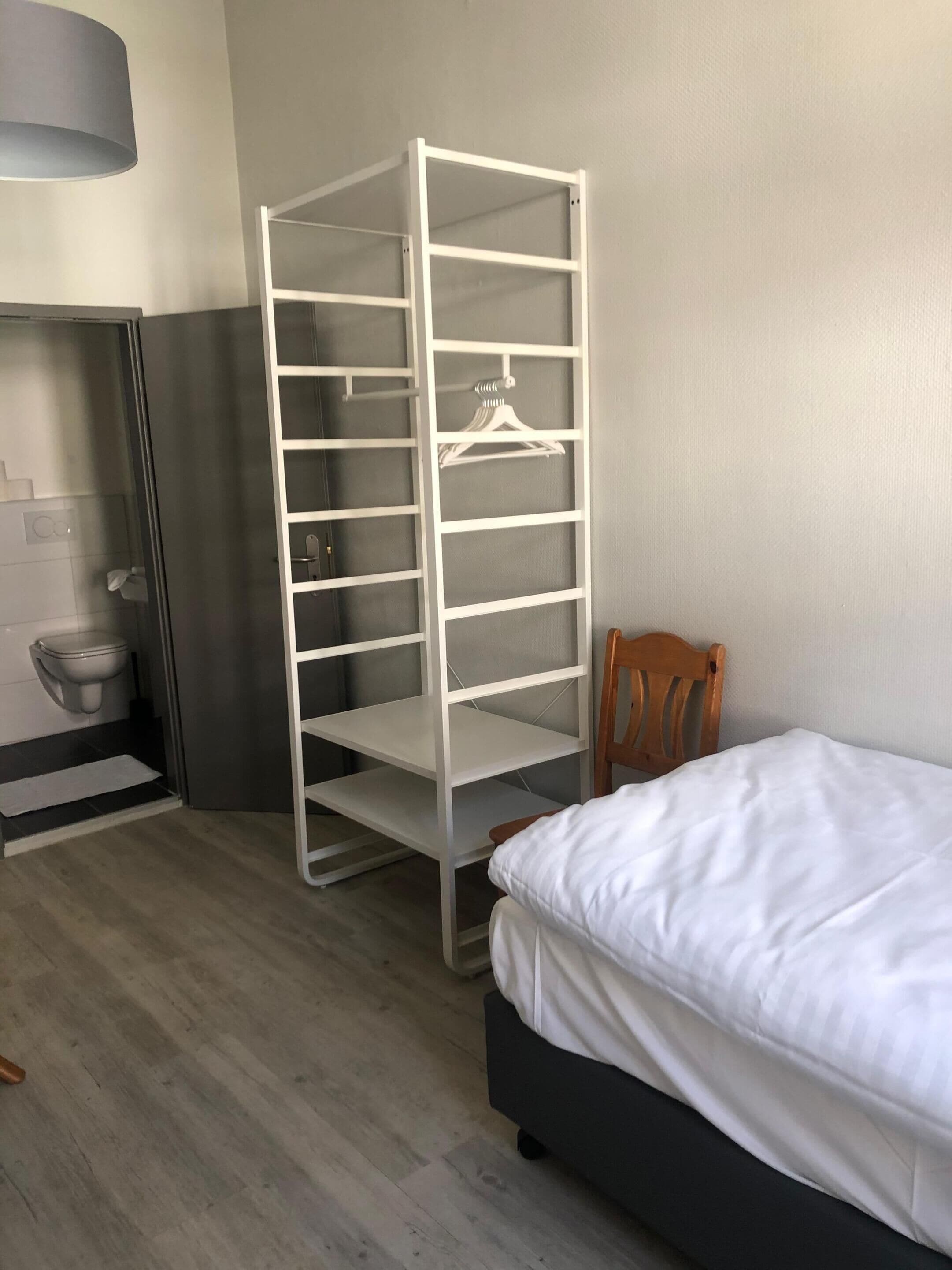 Een kamer met een bed, een houten stoel, een witte kast en een toilet.