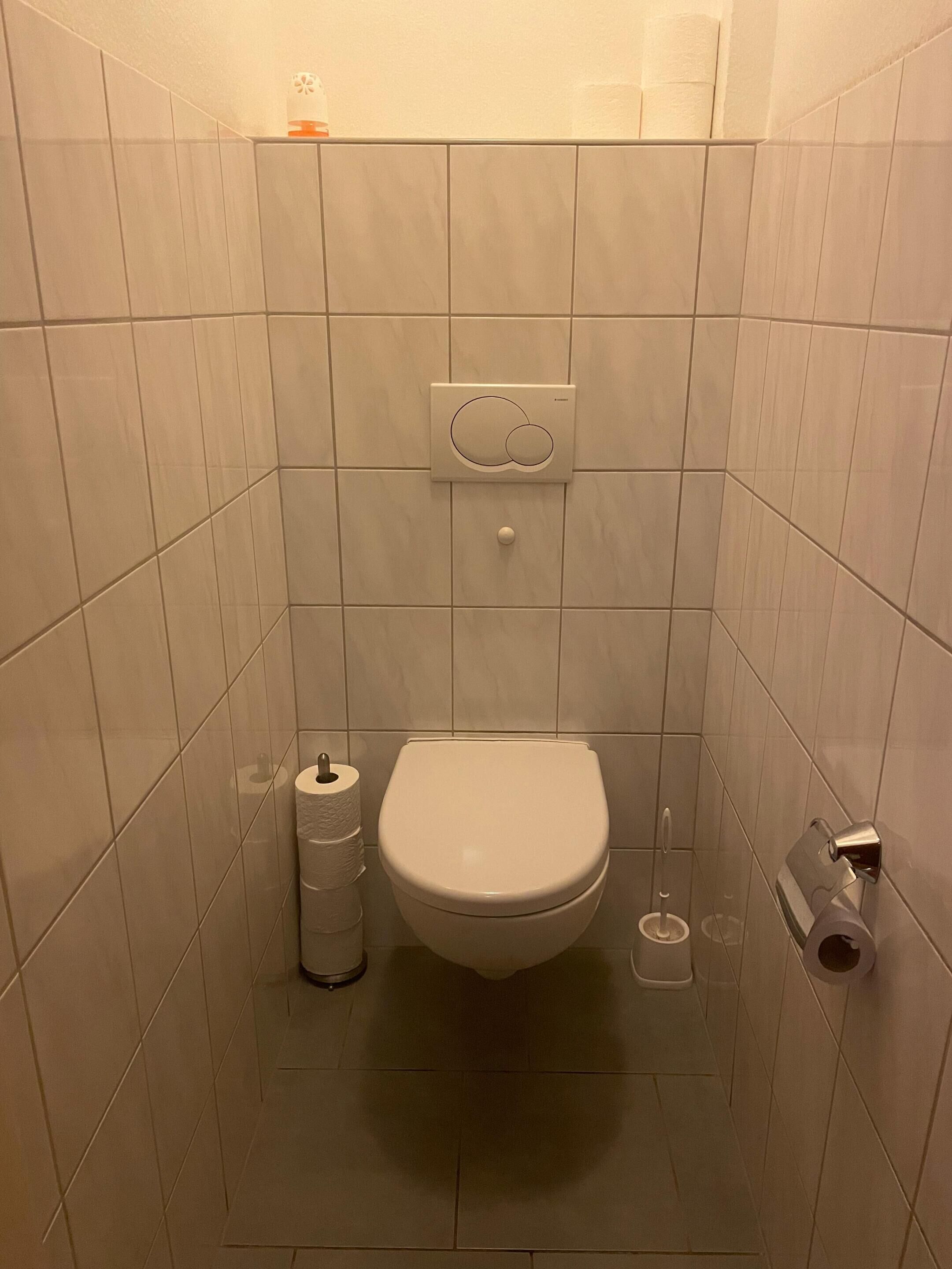 Ett litet badrum med kakel på väggarna, utrustat med en toalett, en toalettpappershållare och en bidé.