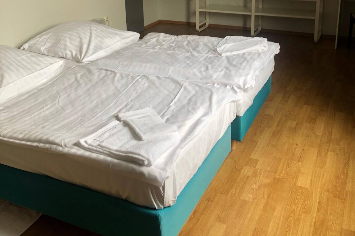 Quarto com duas camas, piso de madeira e escada branca encostada à parede.