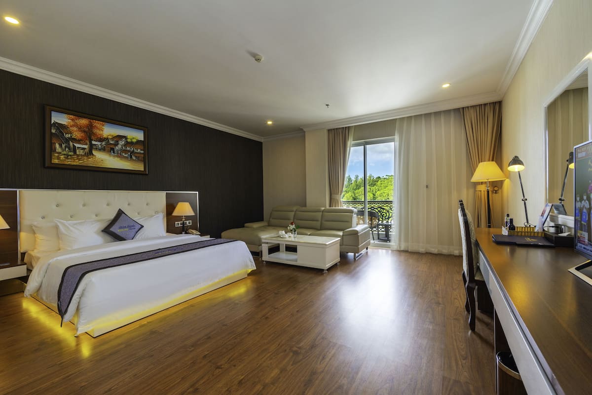 Een hotelkamer met een groot bed, een bank, een bijzettafeltje en een balkon met gordijnen.