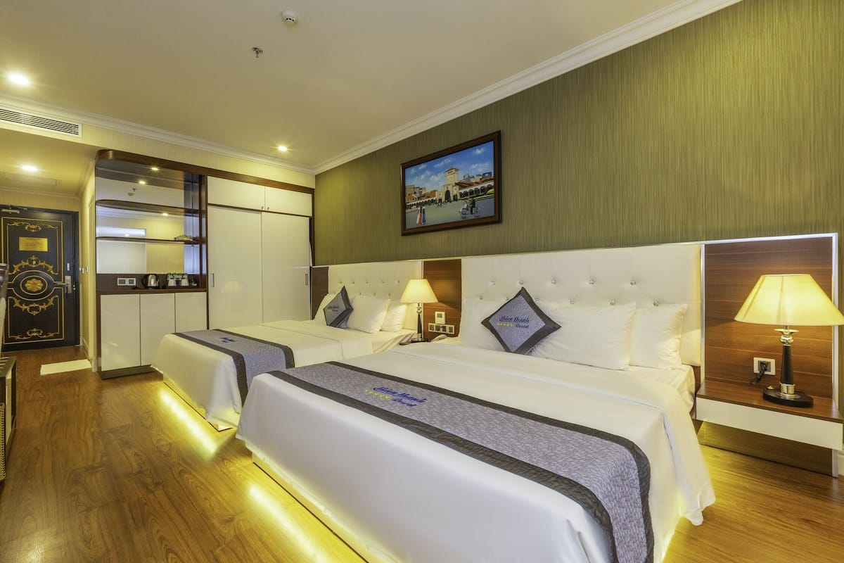 Een hotelkamer met twee bedden, een klein keukenhoekje, een houten vloer en een schilderij aan de muur.