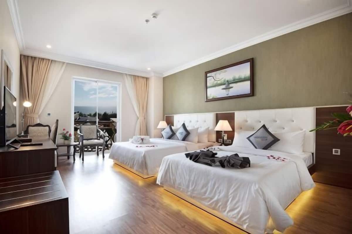 A hotel room with two beds, a desk, a chair, and a large window with a view.