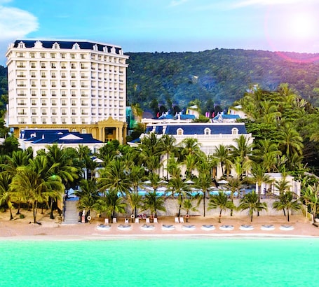 A beachfront hotel with multiple floors, a pool area, and palm trees.