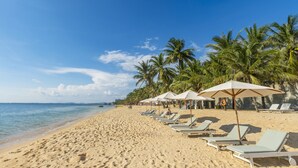 A beach with rows of sun loungers and umbrellas, palm trees, and a clear blue sky. - Thien Thanh Resort Phu Quoc (Phu Quoc)