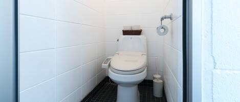 A small, white-walled bathroom with a toilet, a bidet, and a trash bin.