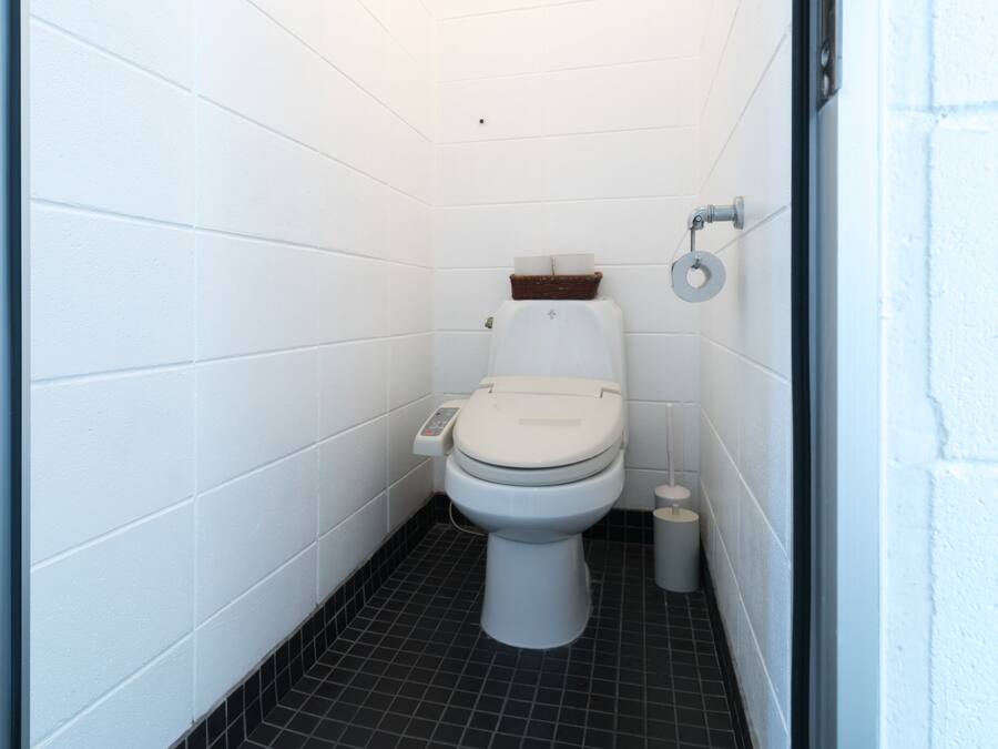 A small, white-walled bathroom with a toilet, a bidet, and a trash bin.