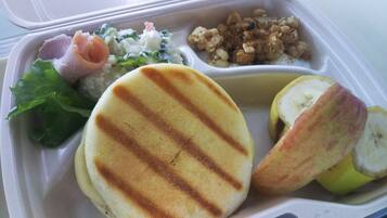 Un repas servi dans un récipient compartimenté, comprenant du pain grillé, une salade et des fruits.