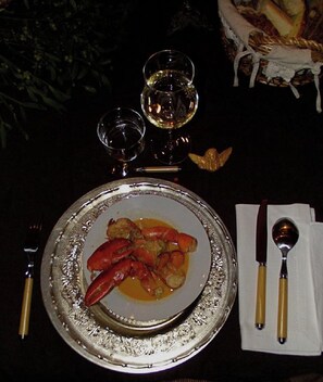 Una mesa de comedor con un plato de langosta, una copa de vino blanco y una cesta de pan.