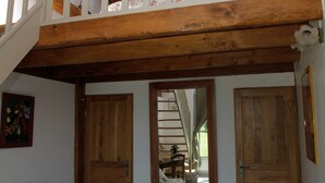 Un dormitorio tipo loft con techo de madera y barandilla blanca. Se observan dos puertas de madera y un espejo en la pared.
