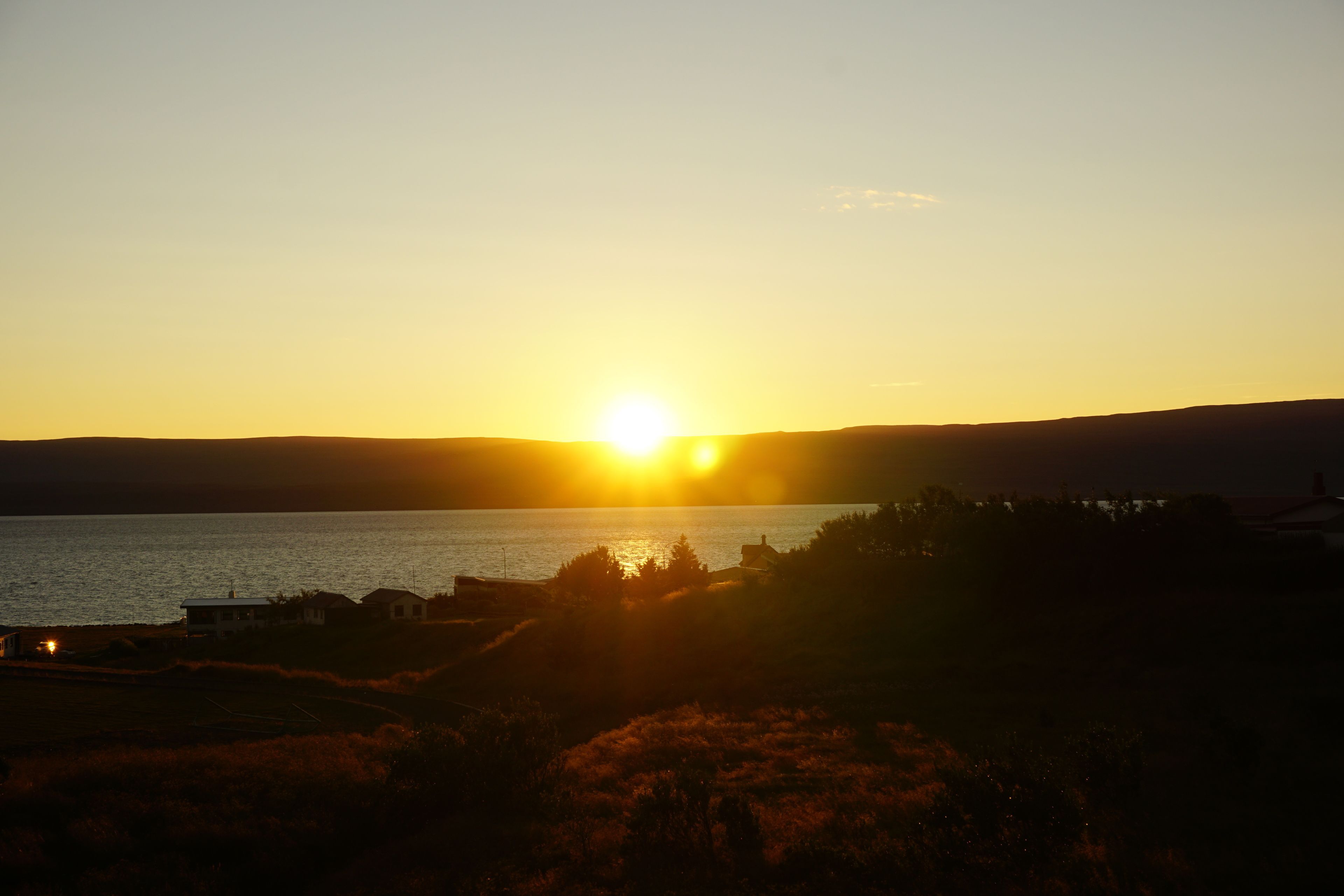 A sunset over a body of water with silhouettes of buildings and vegetation.