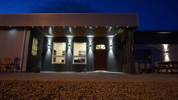 A modern building with a dark facade, large windows, and a covered entrance area. - Dalakot (Budardalur)