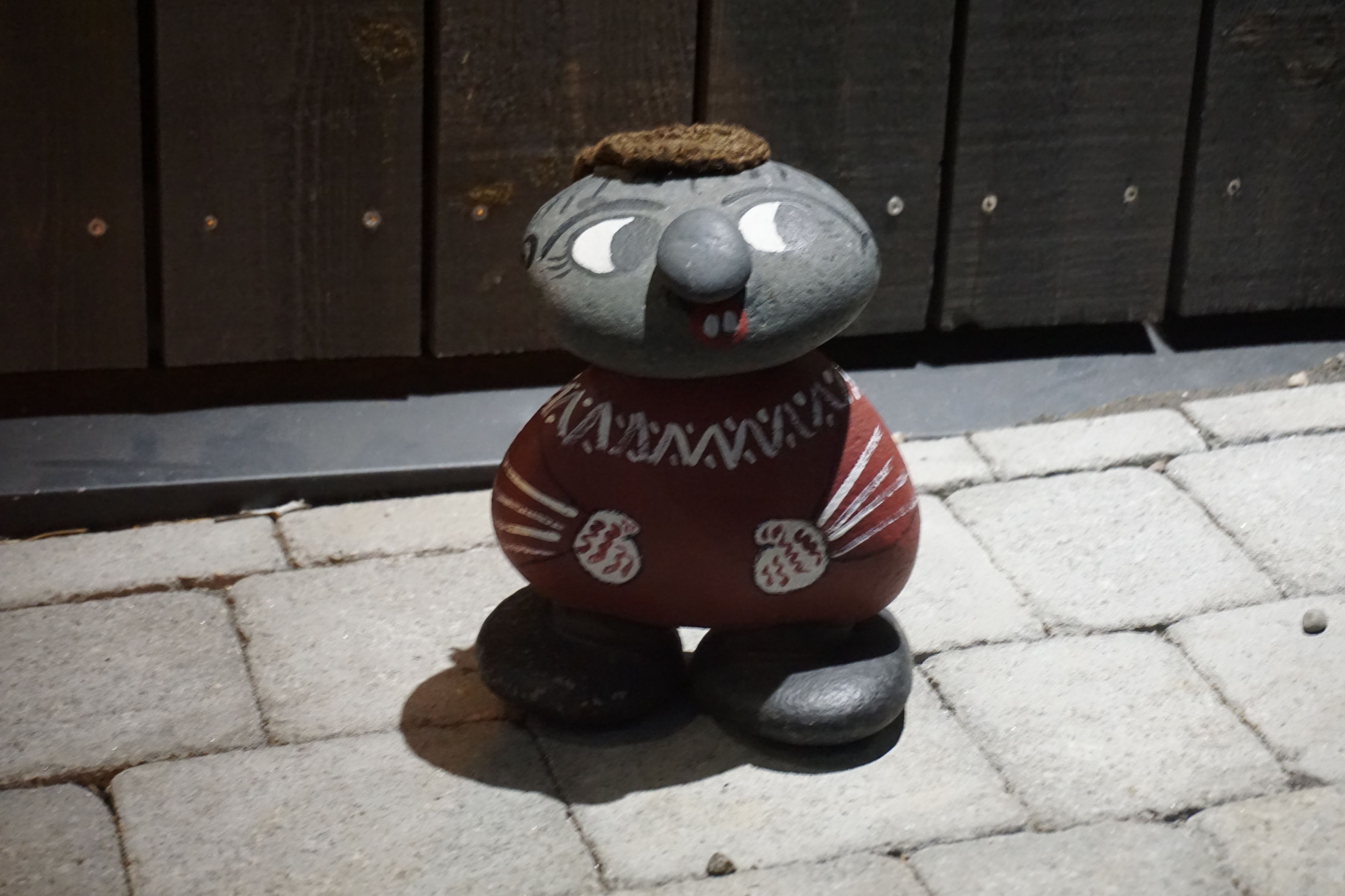 Una estatua de piedra de un oso con una prenda de estampado rojo y blanco, ubicada sobre una superficie pavimentada.