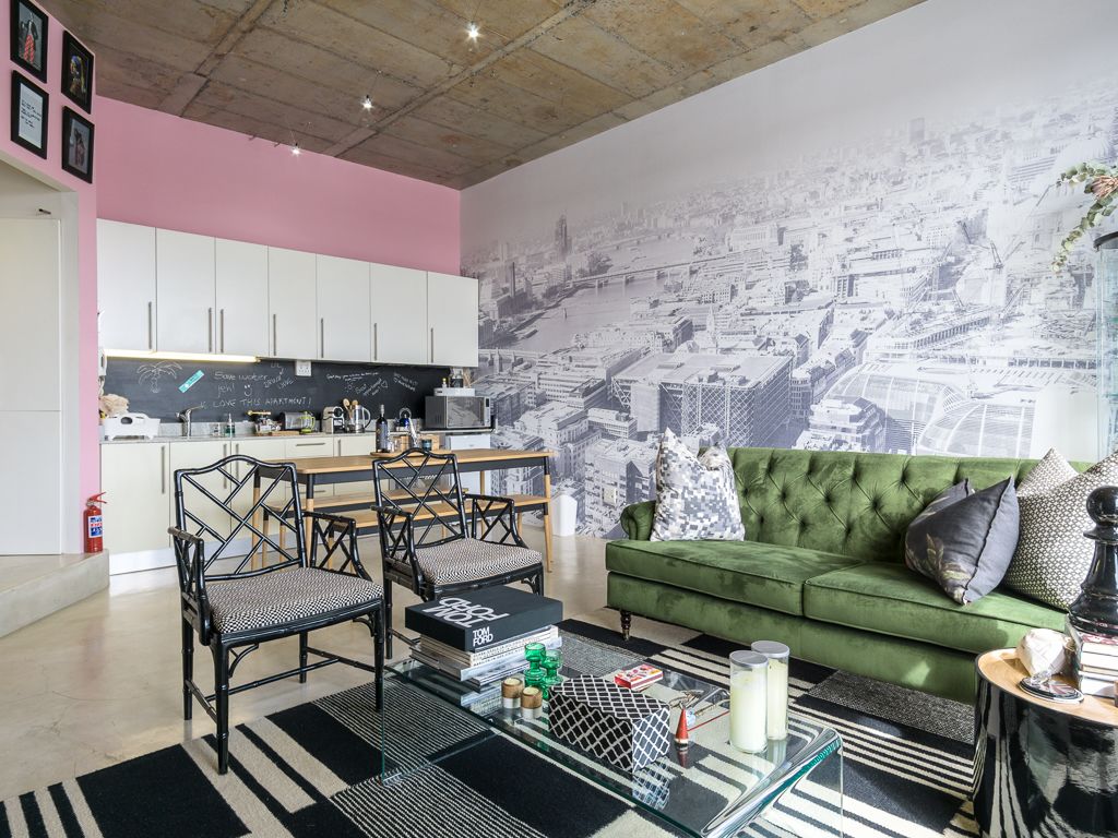 A modern living room with a green sofa, black and white striped rug, and a cityscape mural on the wall.