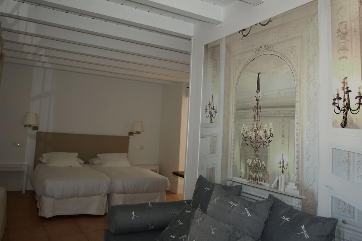 A room with two beds, a sofa, a chandelier, and a decorative mirror.