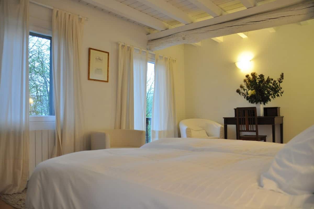 A bedroom with a large bed, a chair, a desk, and a window with curtains.
